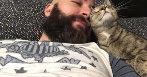 Deze stoere man met ruige baard ligt op bed. Dan komt de kat met hem knuffelen